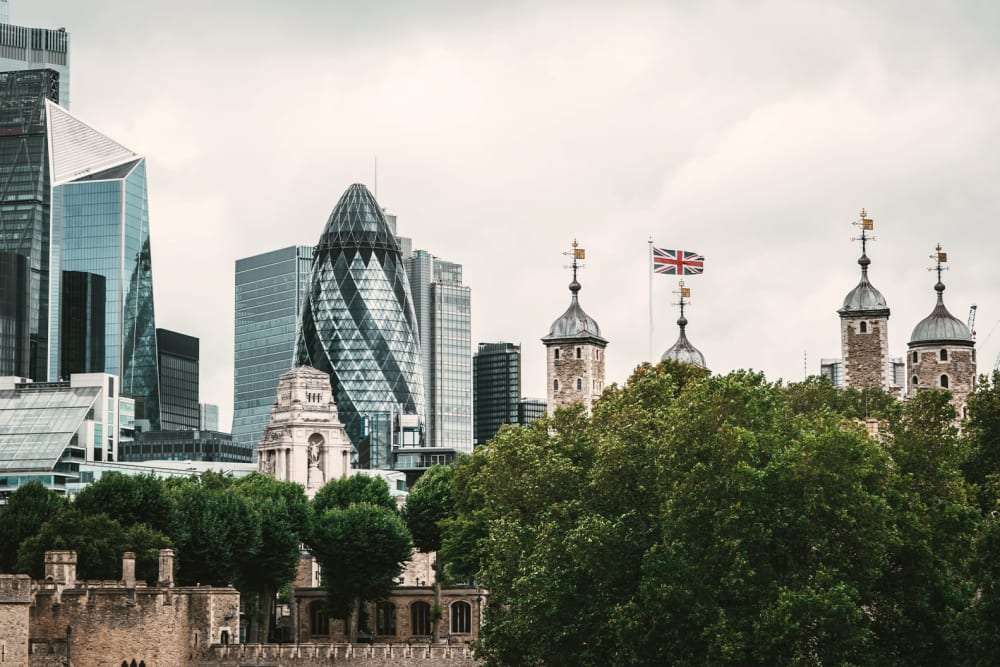 Trees surrounding the Tower of London, with skyscrapers, including the Gherkin, in the City of London in the distance.